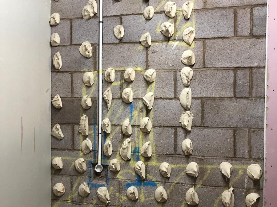 Plasterboard being dot and dabbed onto a blockwork wall